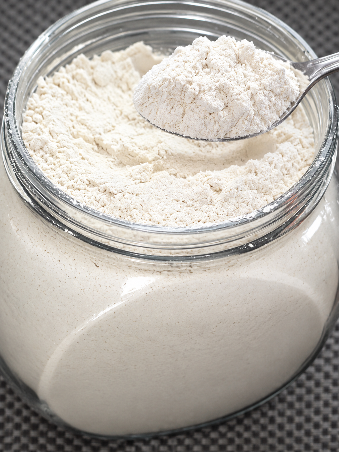 Thni barley flour in a glass jar with a spoon